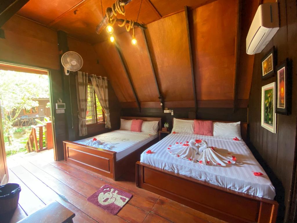 two beds in a room with wooden walls and wood floors at Mondulkiri Pizza Bungalows in Senmonorom