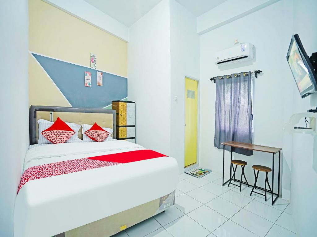 Schlafzimmer mit einem Bett mit roten Kissen und einem Schreibtisch in der Unterkunft OYO 91559 Kost Bangau Syariah in Perabumulih
