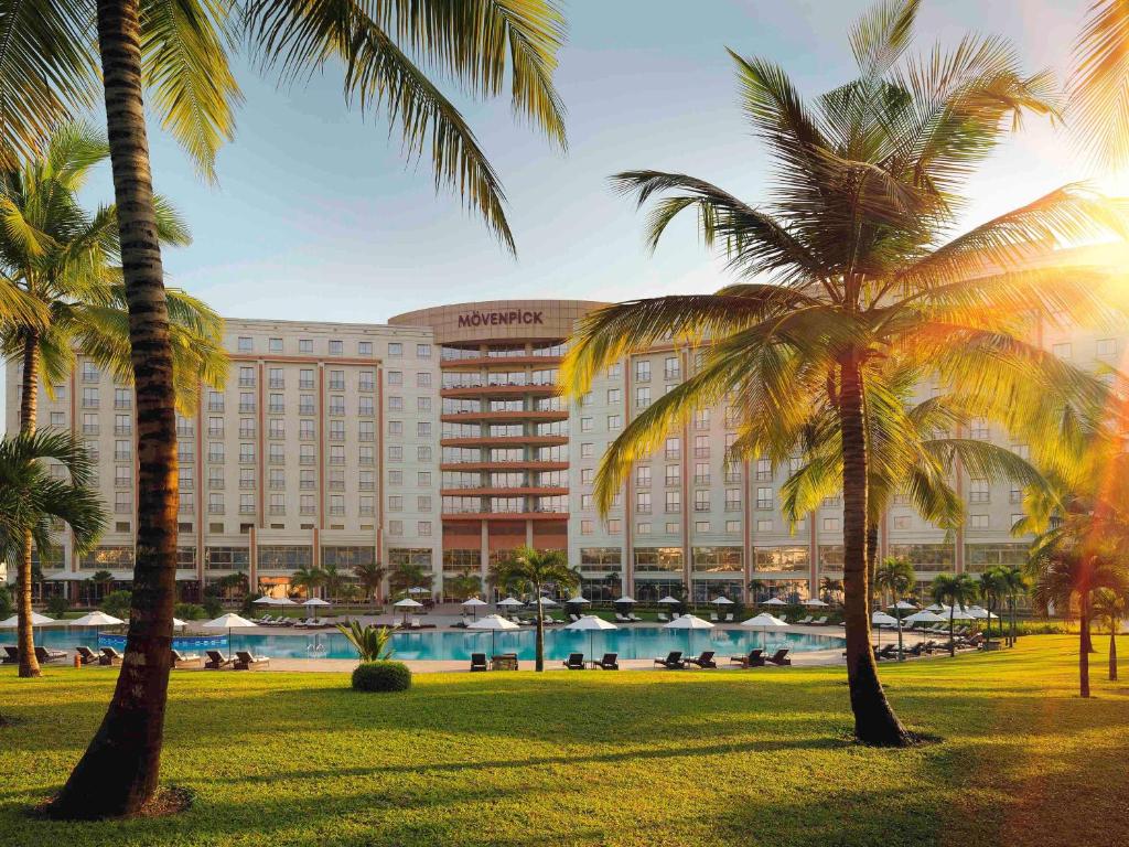 a hotel with palm trees in front of a pool at Mövenpick Ambassador Hotel Accra in Accra