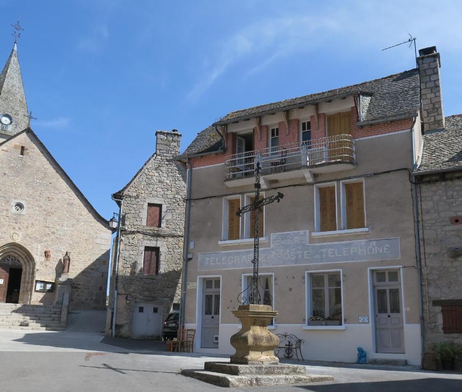 un viejo edificio con una cruz delante de él en L'Ancien Poste, en Sénergues