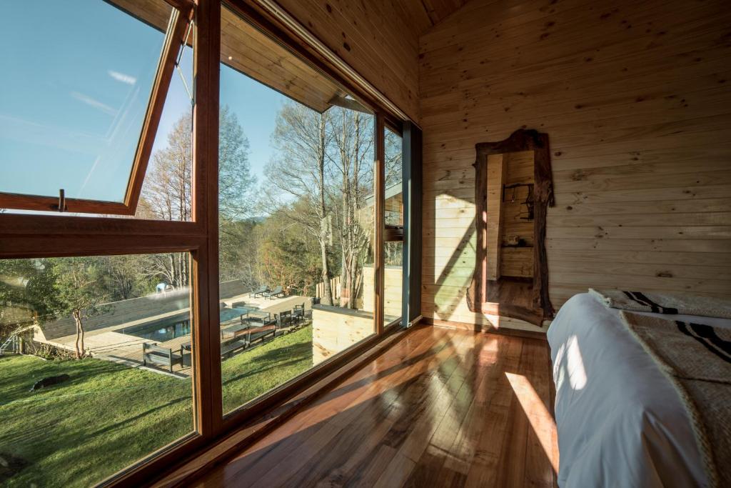 a bedroom with large windows in a wooden house at NI-NEWEN Hotel & Lodge in Pucón