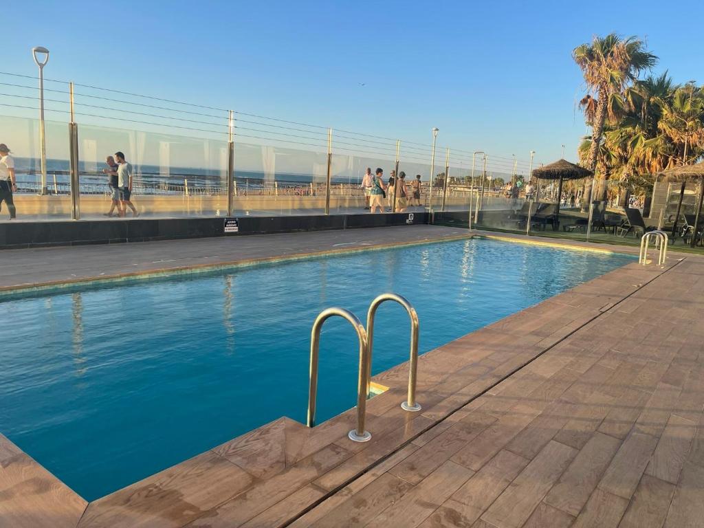 una piscina junto a la playa con gente caminando en Apartamento con piscina en el Paseo Cruz del Mar, en Chipiona