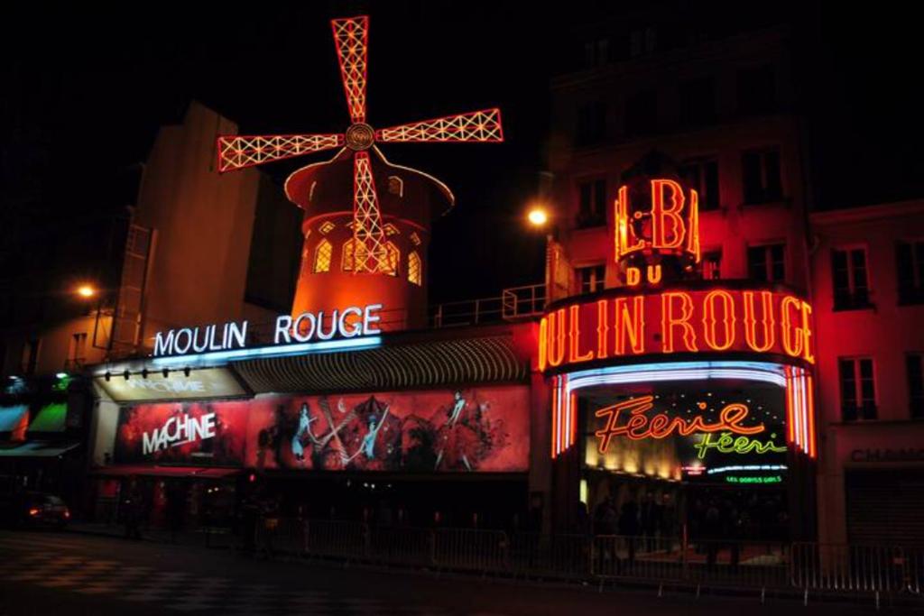 巴黎的住宿－* Moulin Rouge Getaway * 1BR + Desk + Gym weights，一座有 ⁇ 虹灯标志的建筑,上面有风车