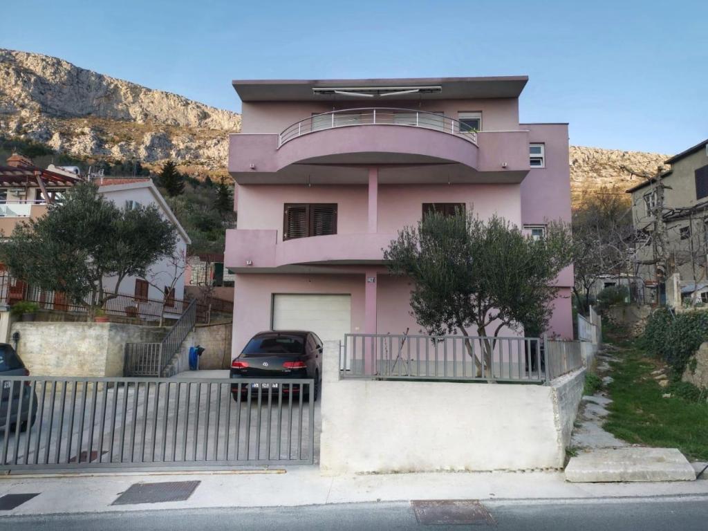 une maison rose avec une voiture garée devant elle dans l'établissement Apartments with a parking space Klis, Split - 16670, à Solin