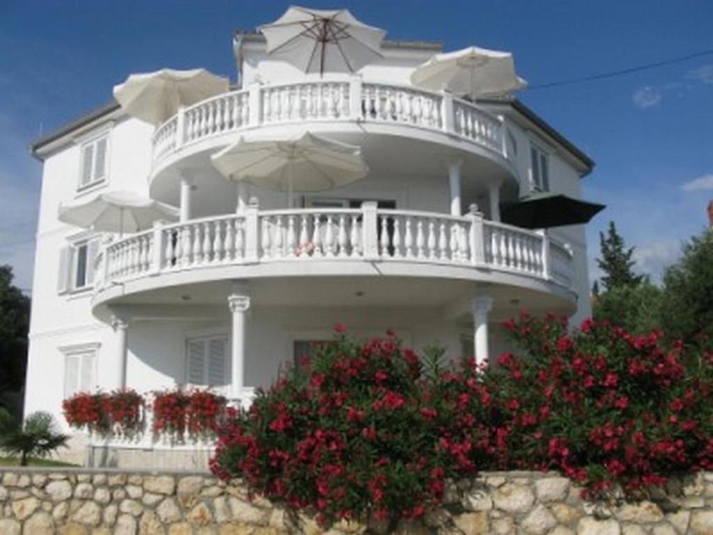 a white house with a balcony with umbrellas at Apartments with parking space Barbat, Rab - 16816 in Rab