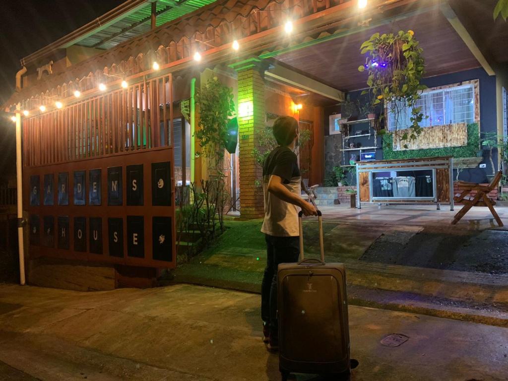Ein Mann steht mit einem Koffer vor einem Gebäude in der Unterkunft Gardens House, Airport Juan Santamaría, Alajuela, San José in Alajuela
