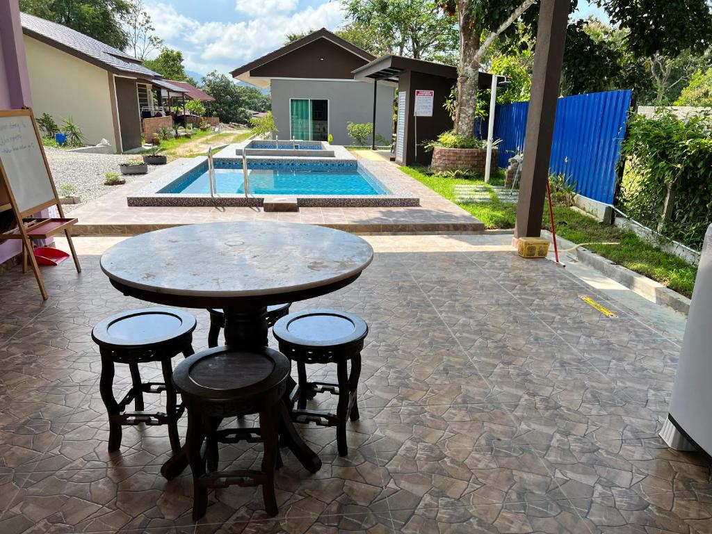 a table and four stools on a patio with a pool at Tok Abu Heritage Roomstay in Pantai Cenang