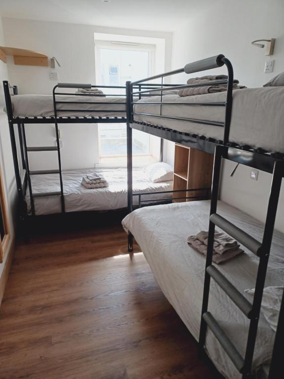 a room with three bunk beds and a wooden floor at Voyage Hostel - Rooms with Shared Kitchen in Douglas