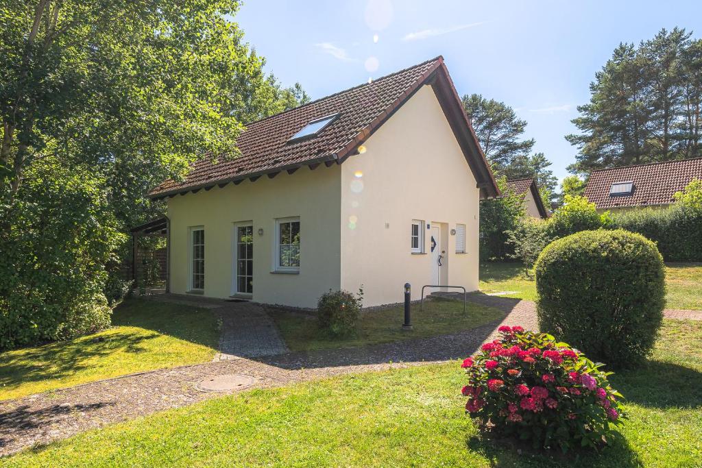 een klein wit huis in een tuin met bloemen bij Ferienhaus Zander im Ferienpark Lenzer Höh in Funfseen