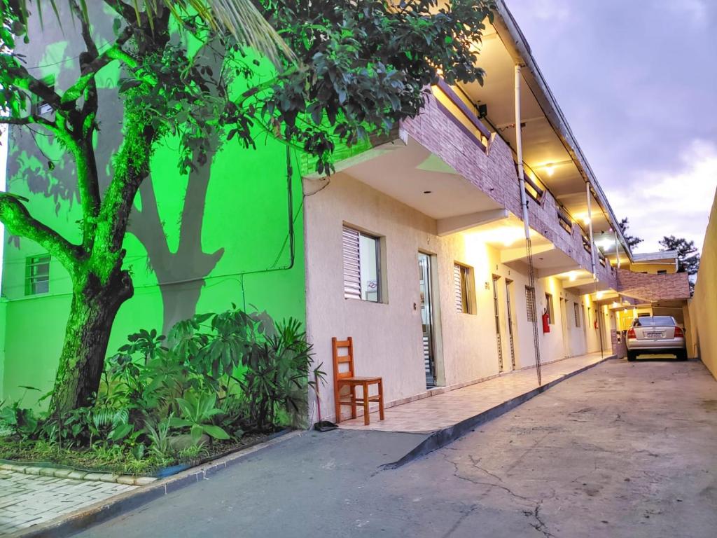 a green and white building with a tree and a chair at Pousada Aconchego in Peruíbe