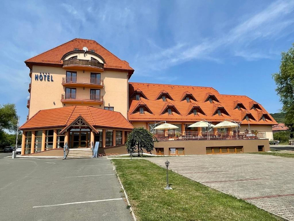 a large building with an orange roof and a parking lot at Hotel Ondava in Stropkov