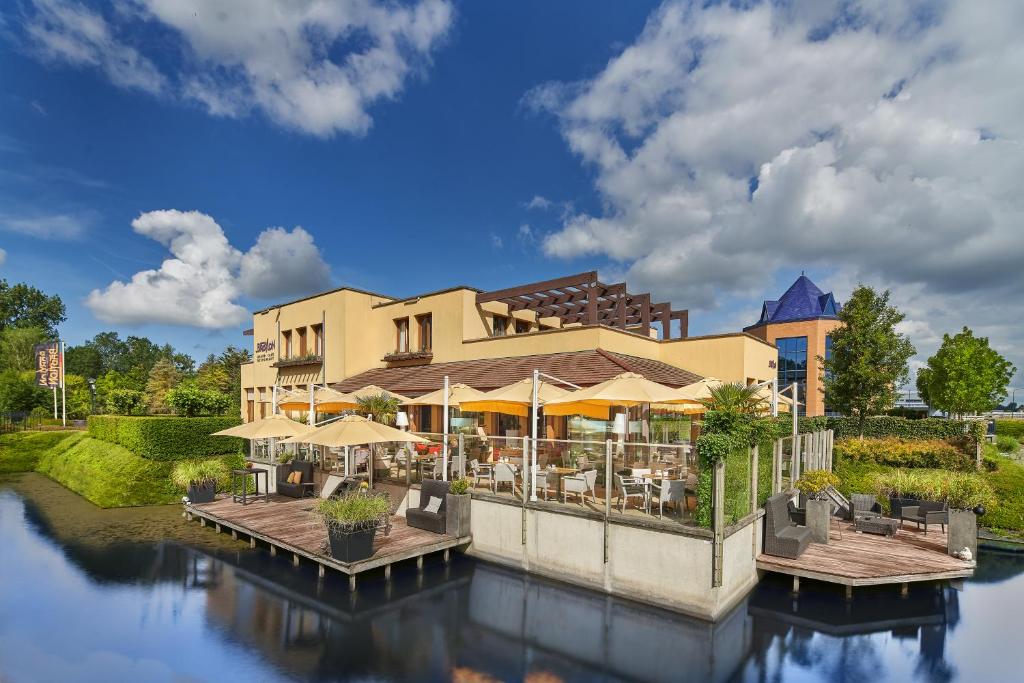 a building with tables and umbrellas next to a river at Hotel Babylon Heerhugowaard - Alkmaar in Heerhugowaard