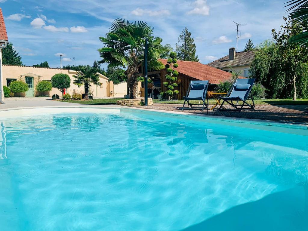 a large swimming pool with two chairs in a yard at Les chambres du Bonheur in Fontaine-sous-Jouy