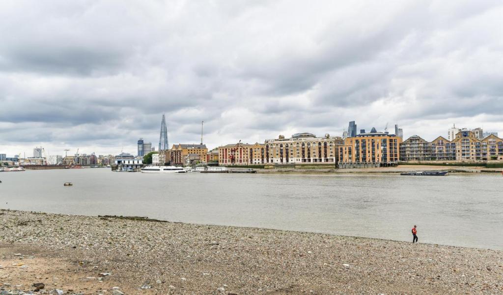 a person standing on the shore of a river with buildings at Modern 4 bedroom Terraced House by the Thames in London