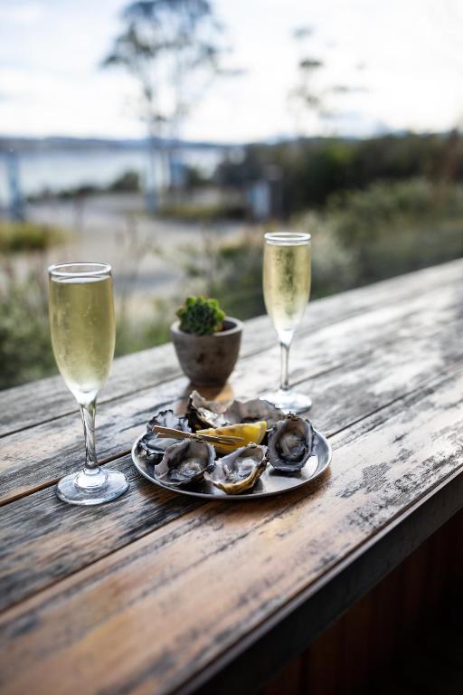 two wine glasses and a plate of oysters on a wooden table at Bruny Island Oceanfront Luxe Cabin with Spa in Adventure Bay