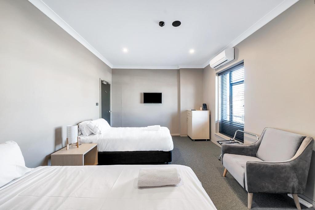 a hotel room with two beds and a chair and a tv at Illinois Hotel in Sydney