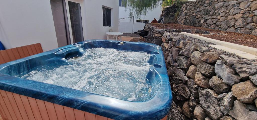 a blue tub filled with water next to a stone wall at Casa Geminis, Relax, Sol y Jacuzzi in Tarajalejo