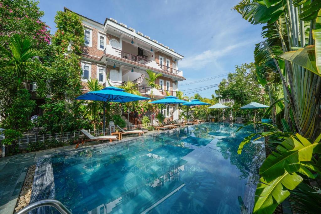 a swimming pool with blue umbrellas and a building at Blooms Boutique Village in Hoi An