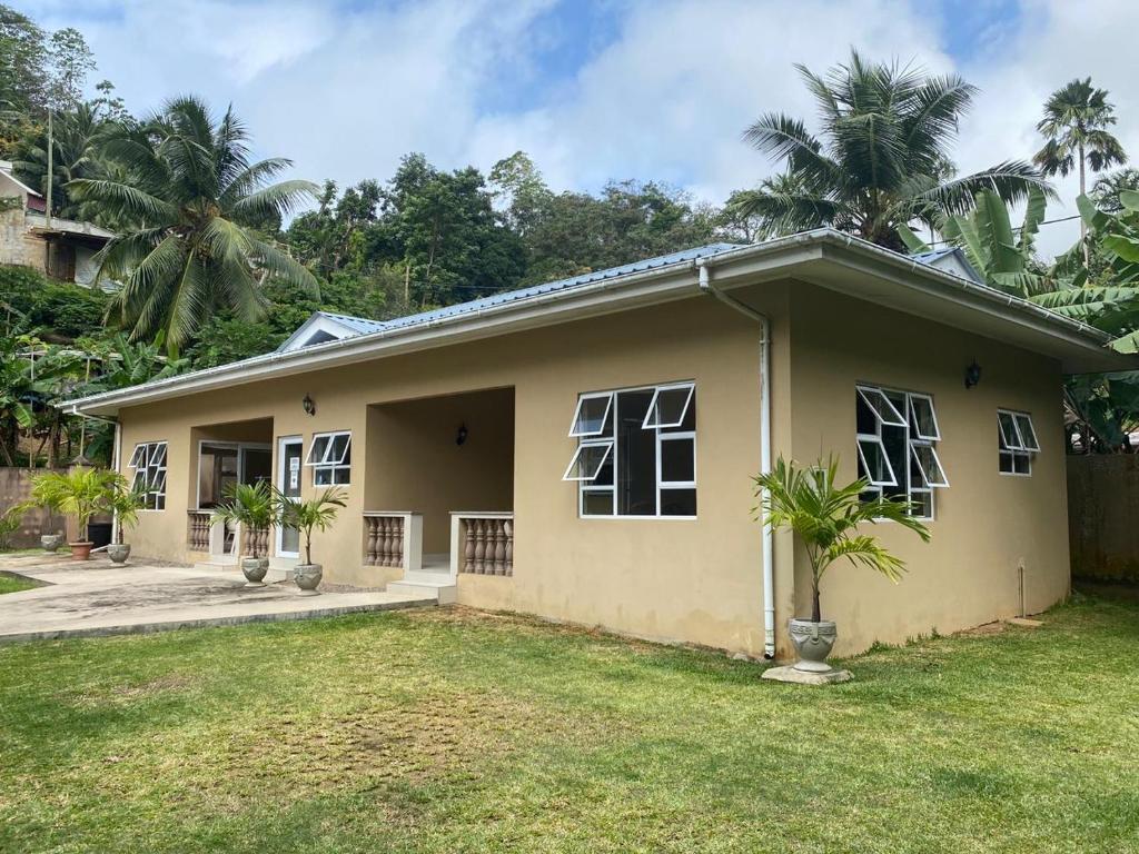 Una pequeña casa amarilla con palmeras detrás. en Beau Bassin Inn, en Baie Lazare Mahé