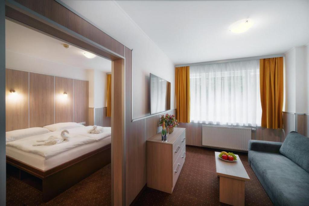 Wellness Hotel GREEN PARADISE في Pirkenhammer: غرفه فندقيه بسرير واريكه