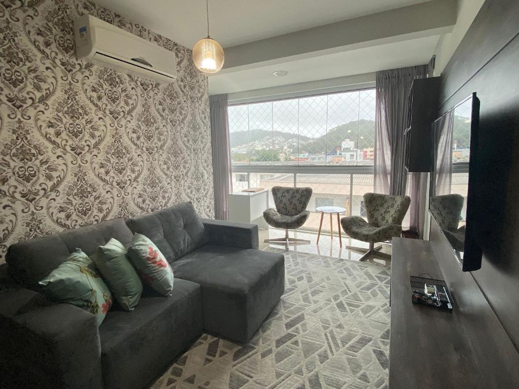 uma sala de estar com um sofá e uma grande janela em Apto luxo e conforto suíte mais dormitório com churrasqueira em Balneário Camboriú