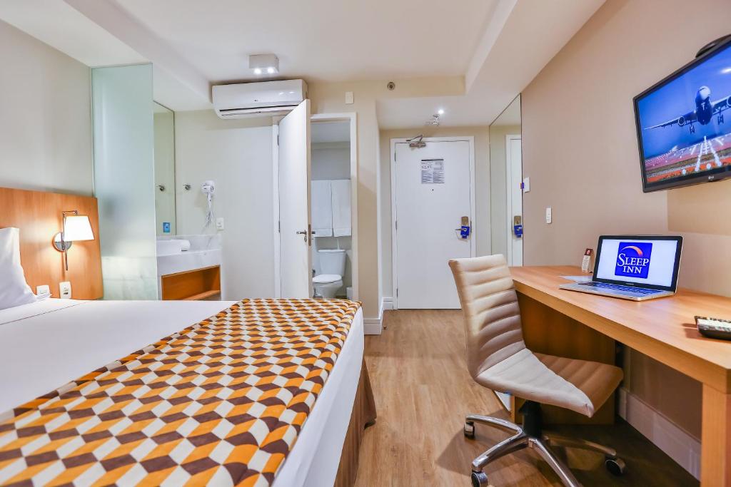 a hotel room with a bed and a desk with a laptop at Sleep Inn Aeroporto de Guarulhos - São Paulo in Guarulhos