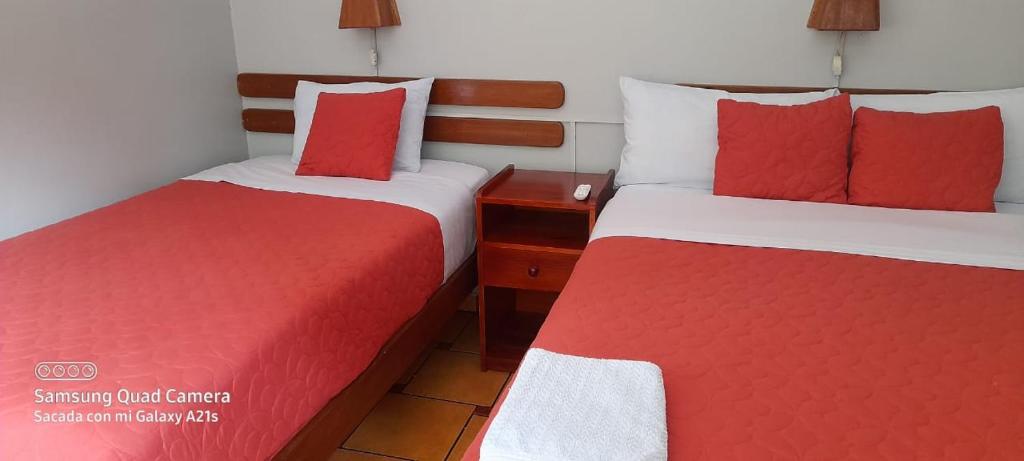 two beds in a hotel room with red and white sheets at Hostal La Payacha in Machu Picchu