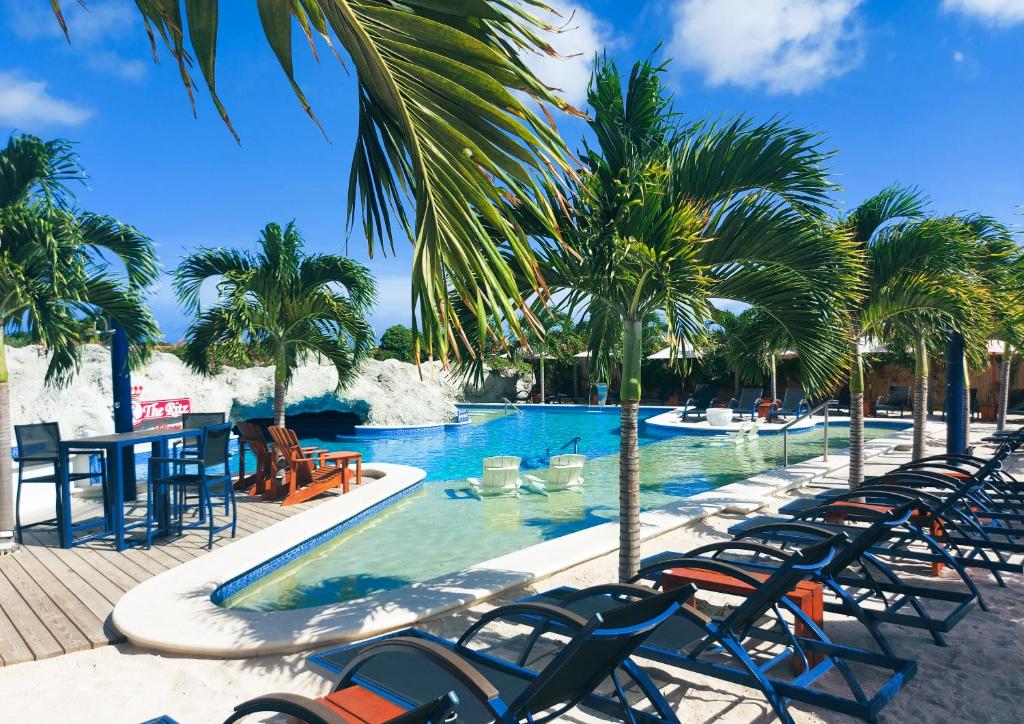 a resort pool with chairs and a table and palm trees at The Ritz Hostel in Willemstad
