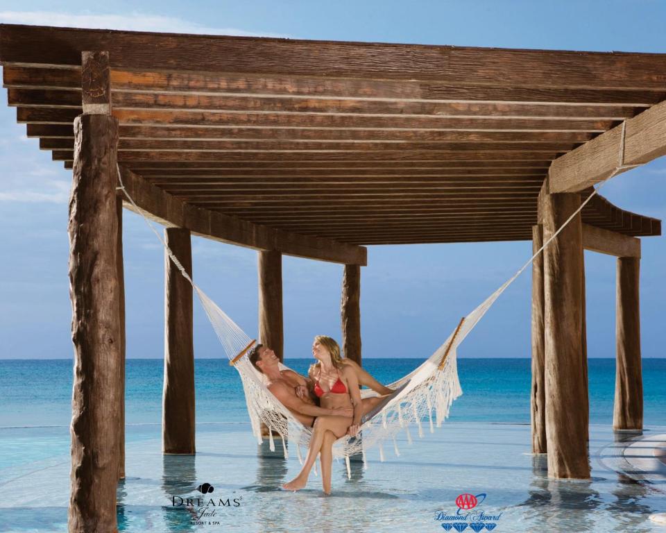 a man and woman sitting in a hammock under a pier at Dreams Jade Resort & Spa - All Inclusive in Puerto Morelos