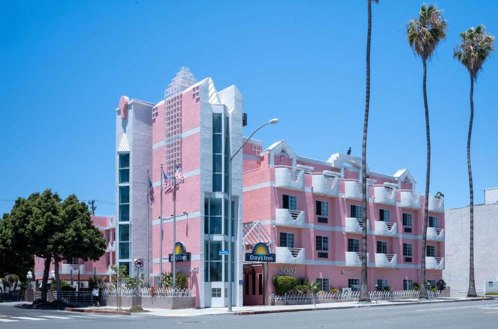 ロサンゼルスにあるDays Inn by Wyndham Santa Monicaのヤシの木が並ぶ道のピンクの建物