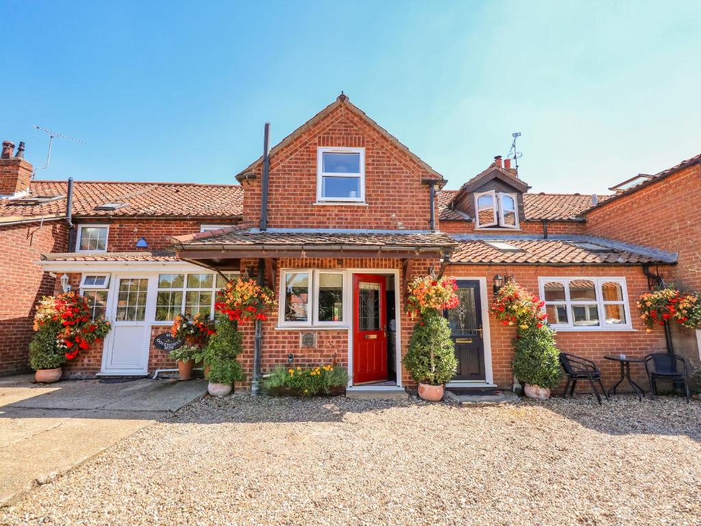 a brick house with a red door and flowers at Cameron's Cottage in Swaffham