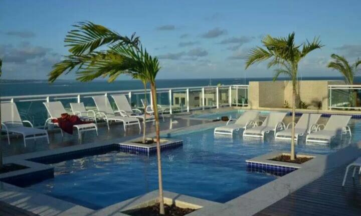 a swimming pool with white lounge chairs and palm trees at Apartamento JTR Maceió in Maceió