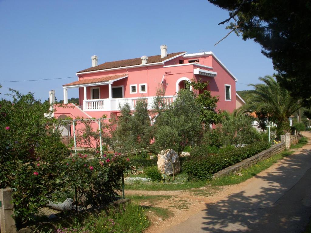 ein rosafarbenes Haus mit Bäumen und Blumen davor in der Unterkunft Apartments by the sea Susica, Ugljan - 841 in Ugljan