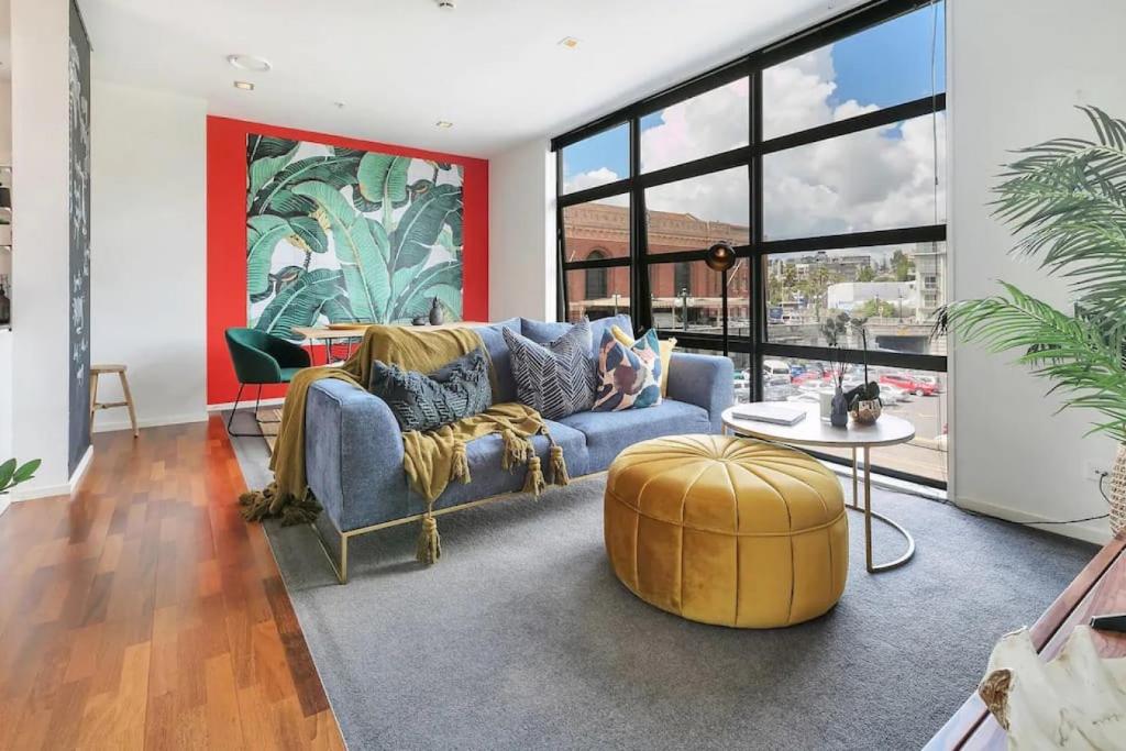 a living room with a blue couch and a large window at Deluxe Mahuhu 2 BR - Spark Arena - FREE PARKING in Auckland