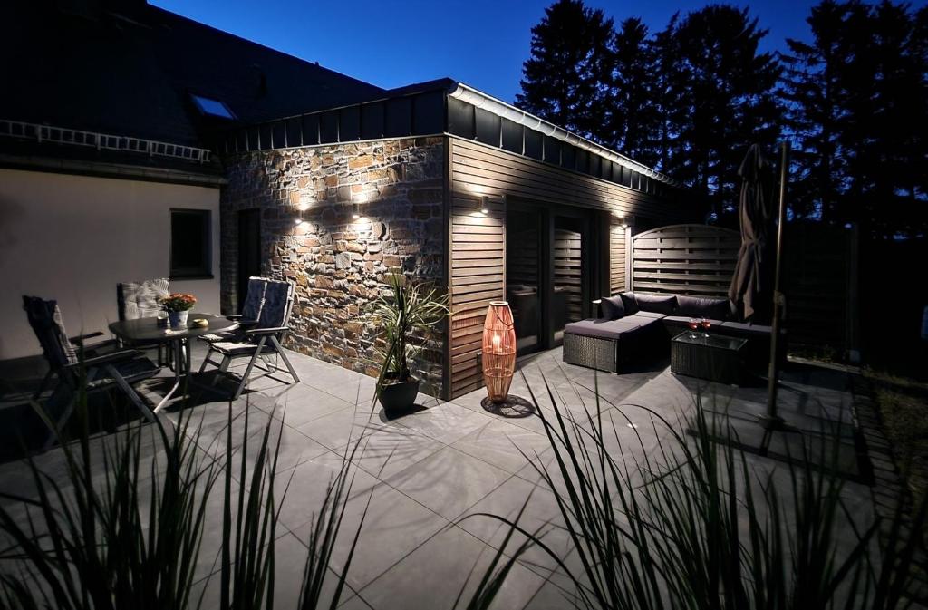 a patio with a table and chairs and a stone wall at Ferienwohnung Kessler's Eifeldomizil in Auw