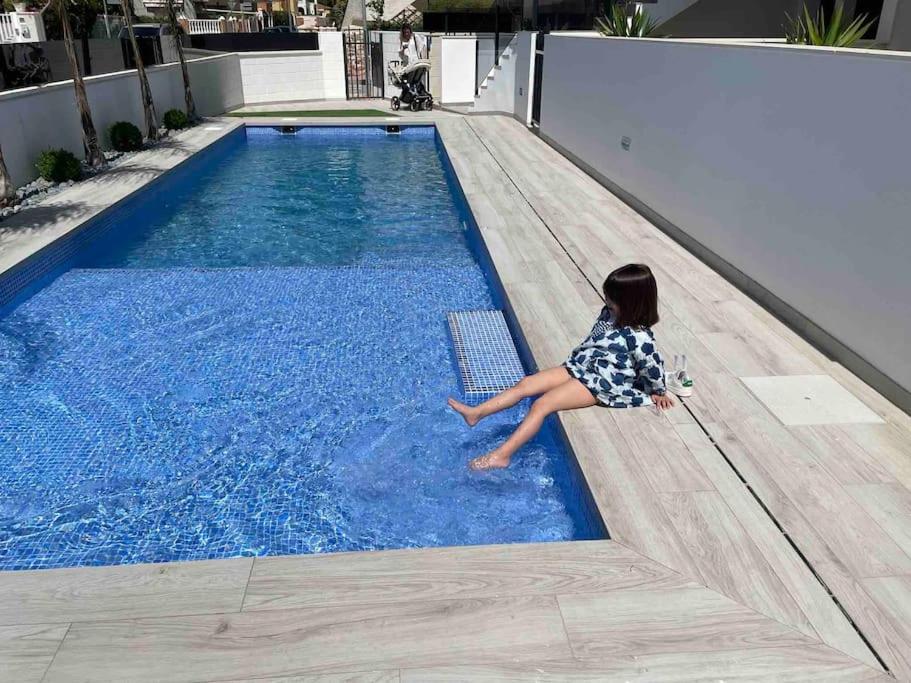 una niñita sentada al lado de una piscina en Beach bungalow with swiming pool and long terrace, en San Javier
