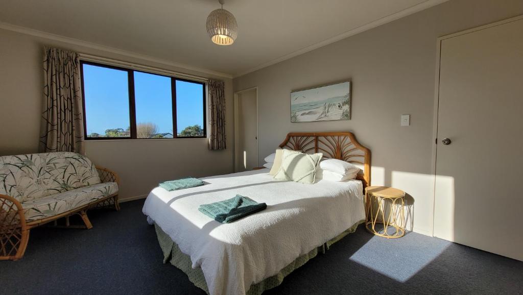 a bedroom with a bed and a couch and a window at Kakariki by the sea in Ngunguru