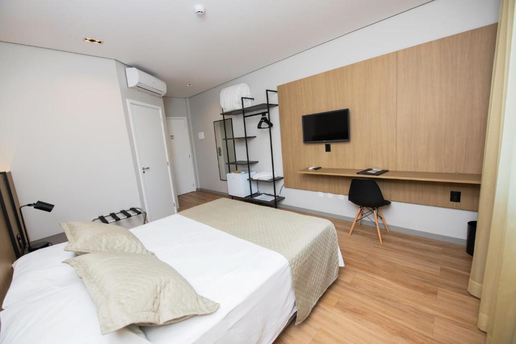 a bedroom with a bed and a desk with a television at Origens Hotel in São Luiz Gonzaga