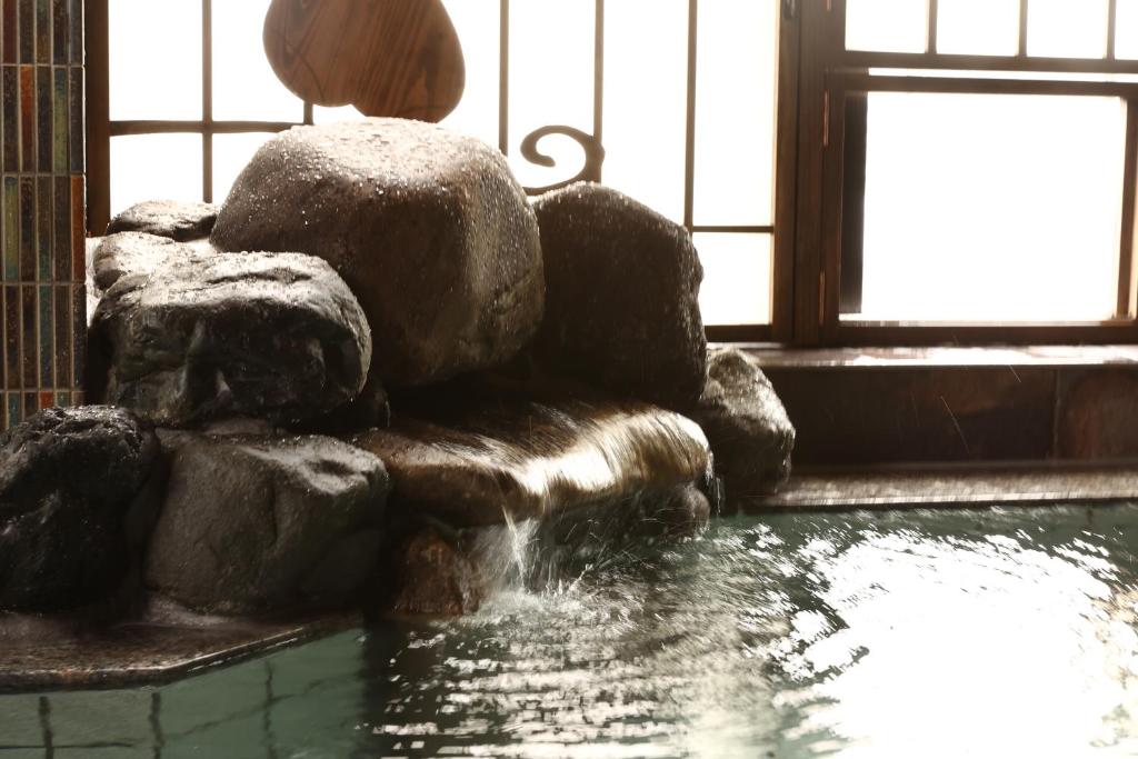Una fuente de agua en una habitación con rocas y una ventana en Dormy Inn Okayama Natural Hot Spring, en Okayama