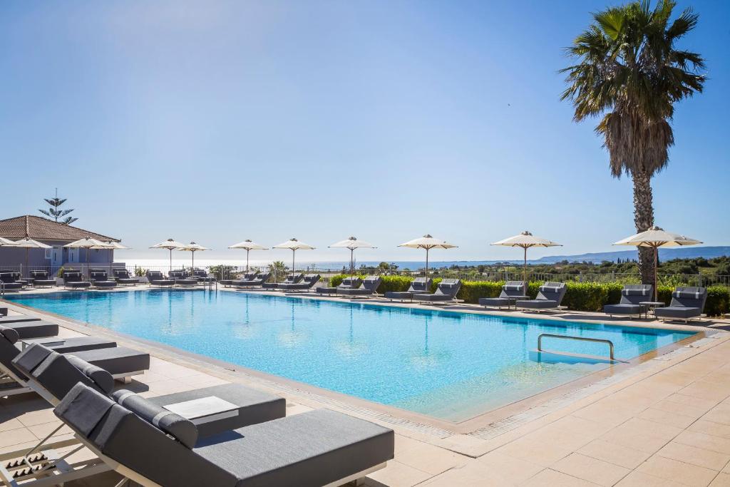 a large swimming pool with lounge chairs and umbrellas at ASTRA Village Resort in Svoronata