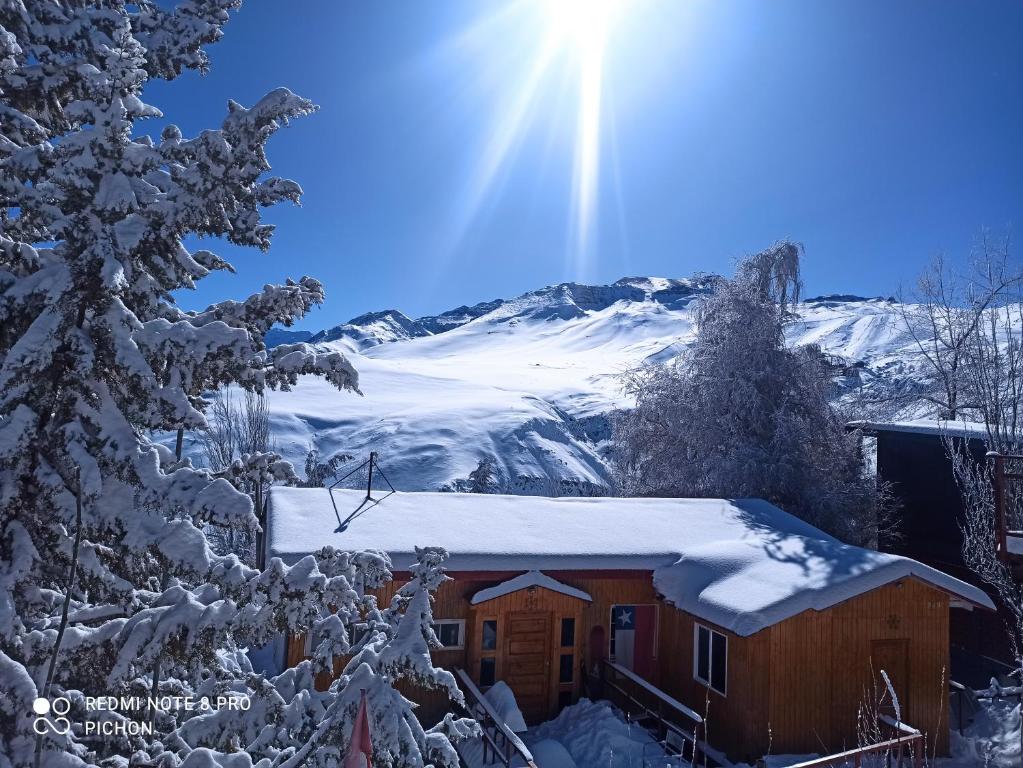 Una cabaña cubierta de nieve con el sol detrás. en Hostal El Pichon en Farellones