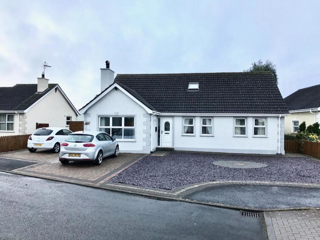 een wit huis met twee auto's geparkeerd op een oprit bij Ty Croeso in Ballymoney