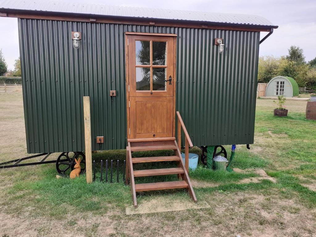 a green shed with a wooden door and a ladder at Glamping in Wiltshire in our luxury Shepherds Hut in Chippenham