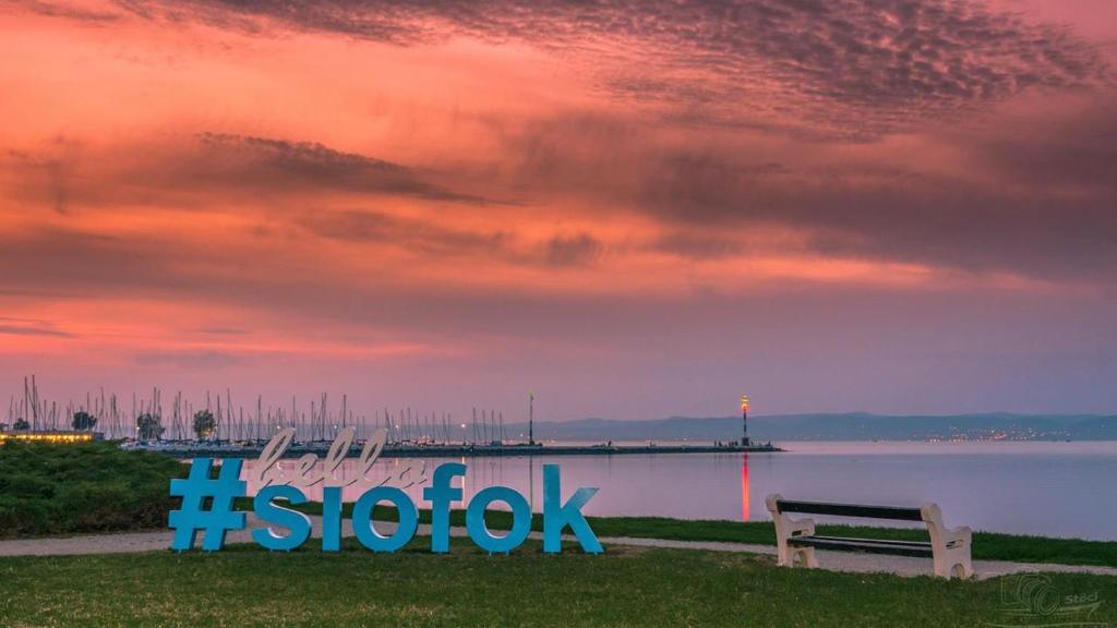un banco sentado junto a un cuerpo de agua con una puesta de sol en Holiday house Riviera - Balaton - Siófok, en Siófok