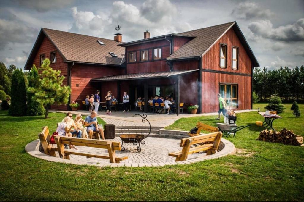 a group of people sitting on benches in front of a house at Kempings Raganas slota in Vārve