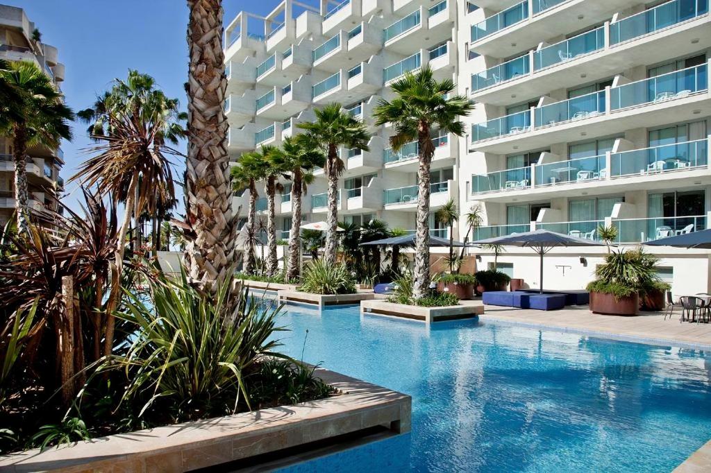 a swimming pool with palm trees in front of a building at Acacias Suites Apartments Salou in Salou
