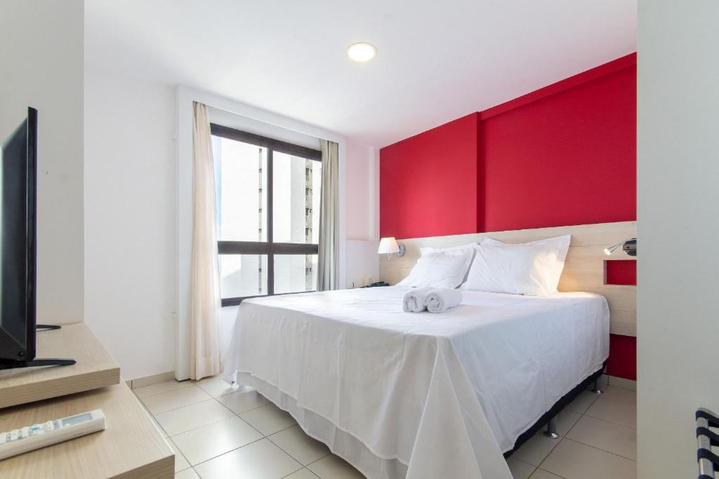 a bedroom with a white bed with a red wall at Suíte Comfort #1004 - em Ponta Negra por Carpediem in Natal