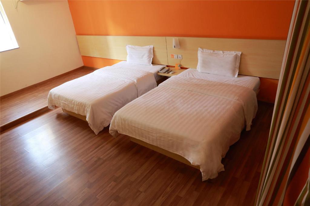 two beds in a room with orange walls and wood floors at 7Days Inn Xi'an High-Tech Electronic City Walking Street in Xi'an