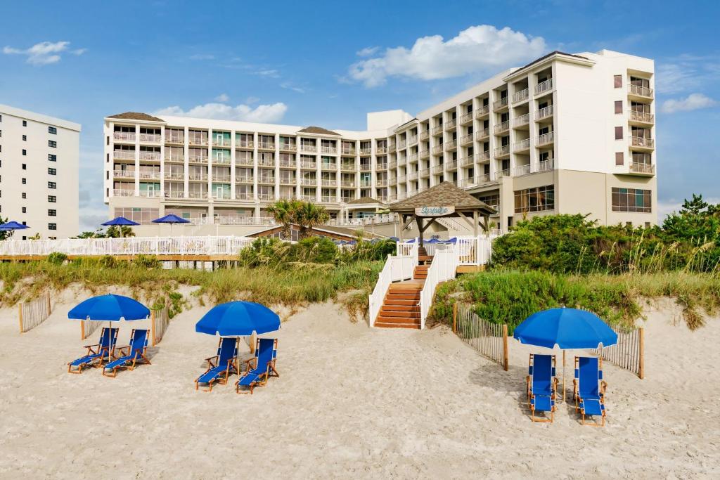 a beach with chairs and blue umbrellas in front of a hotel at Holiday Inn Resort Lumina on Wrightsville Beach, an IHG Hotel in Wrightsville Beach