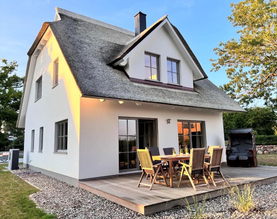 une maison blanche avec une terrasse en bois et des chaises dans l'établissement Ferienhaus Svantovit - exklusives Ferienhaus mit Sauna, Whirlpool und Kamin, à Putgarten